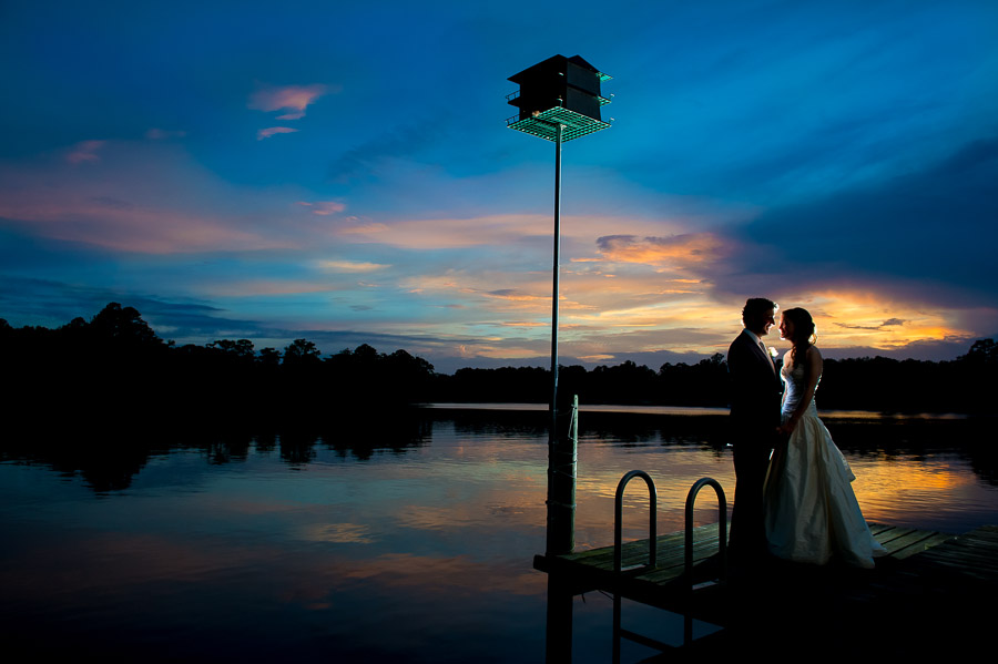 artistic, colorful, stunning wedding portrait of bride and groom on dock at sunset