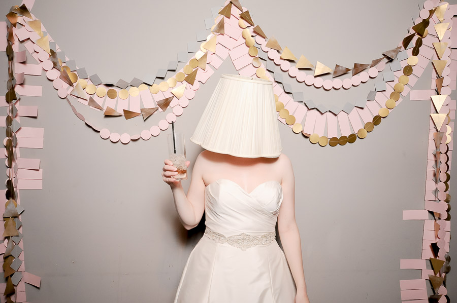 Hilarious photobooth pic of bride with lampshade on her head and geometric paper garland background