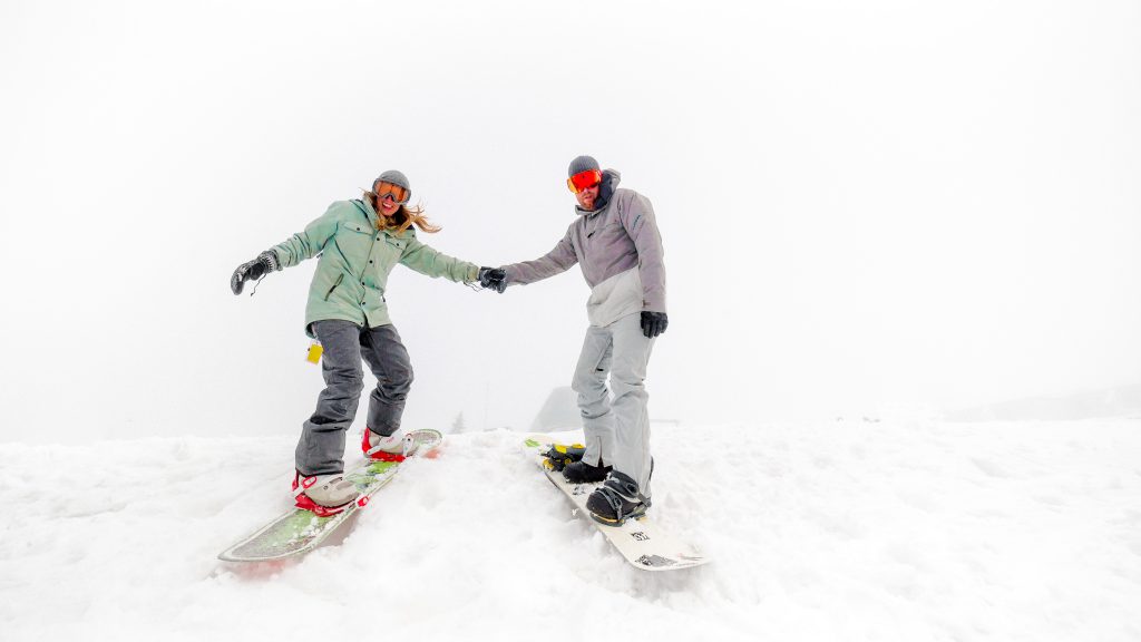 A couple snowboarding downhill holding hands.