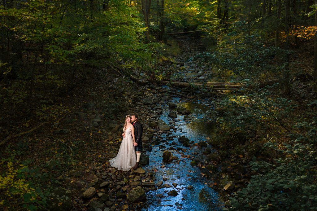 Bride and Groom standing in a river in the middle of the woods at their Nature Camp wedding.