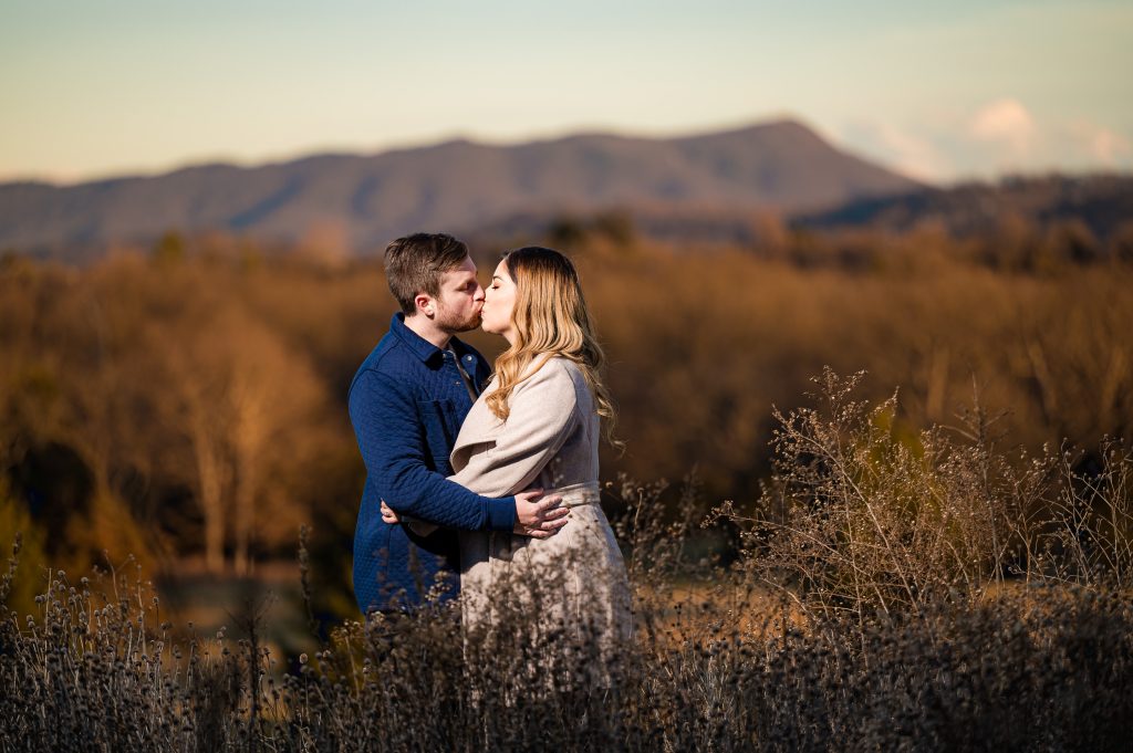 Couple kissing with Massanutten Mountain behind them during their downtown Harrisonburg engagement photography