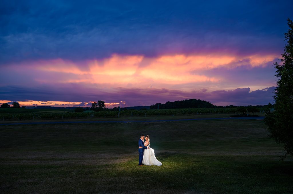 Backlit and spotlight couple in a field in front of the vines and a dramatic sunset at their CrossKeys Vineyards wedding