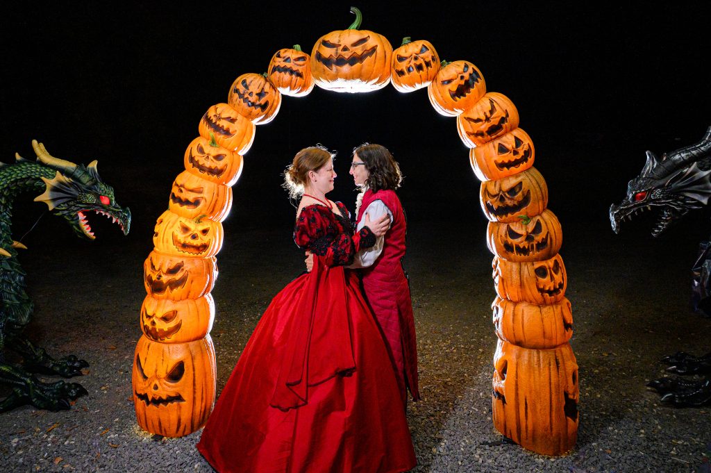 Nighttime portrait of couple at their halloween themed wedding photography in front of a pumpkin arch