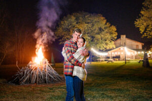 Couple in front of a bonfire at their T + J's lovely, colorful, laid back, outdoorsy, fall Wilderness Adventure at Eagle Landing wedding photography in New Castle, VA.